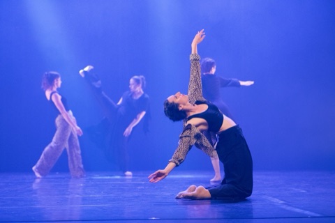 Danseuse en cambré au sol, éclairage bleu, danseurs en fond
